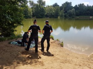 Dwóch funkcjonariuszy rozmawia z ludźmi siedzącymi na plaży nad jeziorem