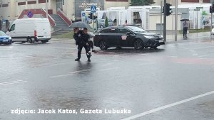 Funkcjonariusz niesie kobietę przez zalaną ulicę.