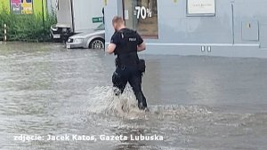 Funkcjonariusz przechodzący przez zalaną ulicę.