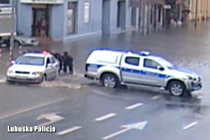 Policjanci zablokowali zalaną ulicę własnym radiowozem i pomagają wypchnąć auto z wody.