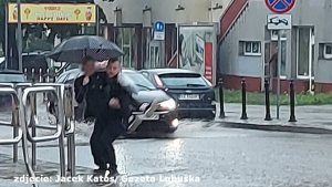 Policjant niosący kobietę przez zalaną ulicę