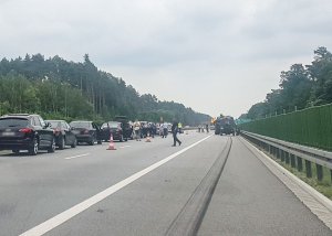 Kolejka samochodów osobowych na drodze szybkiego ruchu znajdująca się na lewym pasie jezdni. Na prawym pasie stoi uszkodzony samochód wojskowy obok niego stoją funkcjonariusze policji.