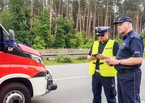 Dwóch funkcjonariuszy rozmawiający przy pojeździe straży pożarnej.