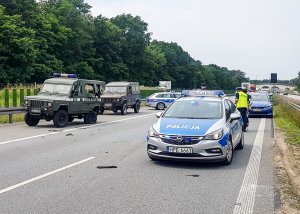 Radiowóz policyjny stojący na tle zakorkowanego lewego pasa jezdni i uszkodzonego samochodu na prawym poboczu.