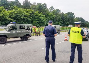 Dwóch funkcjonariuszy stojący obok uszkodzonego zielonego samochodu z napisem &quot;Regulacja Ruchu&quot;.