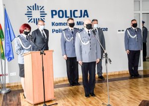 Grupa umundurowanych policjantów ubranych w maseczki ochronne stoją na tle białej ściany z napisem &quot;POLICJA Komenda Miejska Policji w Zielonej Górze&quot;, dwoje policjantów stoją przy mikrofonach.