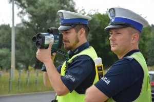 Dwóch umundurowanych policjantów w średnim wieku, jeden trzyma czarny laserowy miernik prędkości, a drugi żółty alkomat.