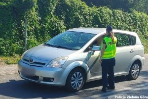 policjantka w odblaskowej kamizelce stojąca tyłem kontroluje trzeźwość kierującego siedzącego w srebrnym samochodzie