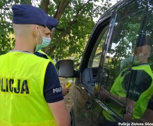 policjant w kamizelce odblaskowej i furażerce sprawdza trzeźwość kierującego urządzeniem alcoblow