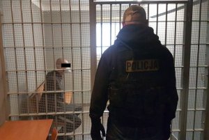 Policjant obserwuje mężczyznę który siedzi za kratami