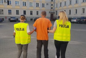 Policjanci w kamizelkach odblaskowych prowadzą zatrzymanego mężczyznę