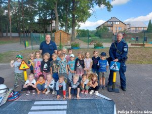 Policjant i policjantka z grupą dzieci obok edukacyjnego miasteczka ruchu drogowego