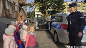 Policjantka stojąca przed radiowozem wraz z grupą dzieci.