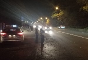 Policjanci stoją przy radiowozie w nocy przy drodze