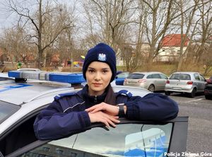 Policjantka stojąca przy radiowozie z rękoma na drzwiach.