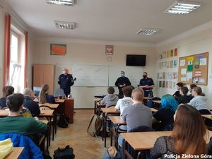 Uczniowie siedzący w ławkach w klasie. Przed ławkami stoją trzej policjanci w granatowych mundurach.