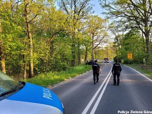 Policjanci zabezpieczają drogę, w tle widać straż pożarną