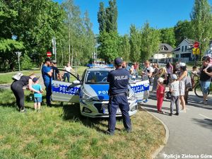 Radiowóz policyjny wraz z grupą cywili oraz policjantami.