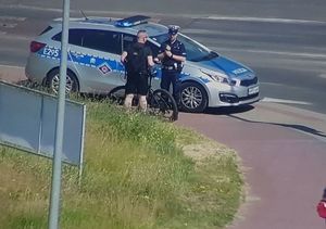 Radiowóz obok którego stoi dwójka policjantów.