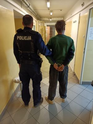 Policjant prowadzi mężczyznę zakutego w kajdanki.