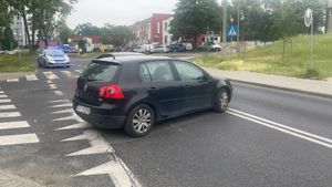 Samochód osobowy marki Volkswagen Golf uczestniczący w zdarzeniu drogowym, w tle radiowóz policyjny z włączonymi światłami błyskowymi.