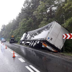 Samochód ciężarowy i osobówka leżąca w rowie,  w tle radiowóz z włączonymi światłami błyskowymi.