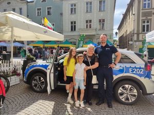 Kobieta wraz z dwójką dzieci stojąca obok umundurowanego Policjanta, w tle radiowóz.