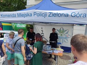 Grupa ludzi stoi obok stoiska Policyjnego. Dwóch funkcjonariuszy promuje zawód policjanta.