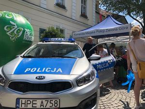 Kobieta z dzieckiem wchodzi do radiowozu, obok umundurowany policjant