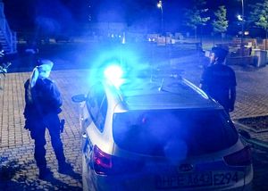 Radiowóz policyjny na sygnale a obok dwójka policjantów.