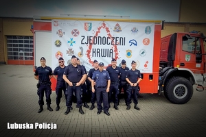 Policjanci przy wozie strażackim z napisem Zjednoczeni krwią