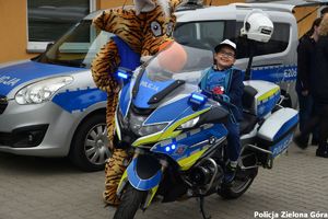 Jasiu siedzący na policyjnym motocyklu a obok maskotka policyjna LUPO.