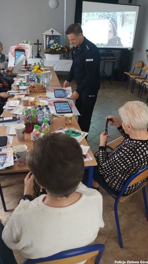 Policjant stojący przy stoliku wraz z Zielonogórskimi seniorami.