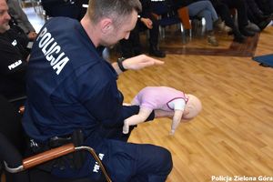 Policjant pokazuje jak poprawnie wykonać RKO małemu dziecku.