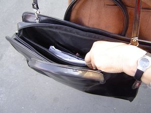 Torebka z portfelem w środku oraz ręka złodzieja wyciągającego portfel