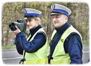 Policjantka i policjant ruchu drogowego mierzą prędkość samochodów przy drodze