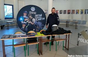 Policjant na stoisku Komendy Miejskiej Policji w Zielonej Górze z ulotkami i upominkami