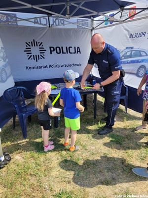 Policjant wręcza dzieciom opaski odblaskowe