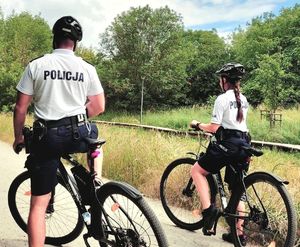 Policjant i policjantka ubrani w białe t-shirty i szorty z napisem POLICJA pełnią służbę na rowerach.