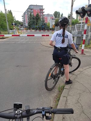 Policjantka pełniąca służbę na rowerze oczekuje na podniesienie rogatek kolejowych.