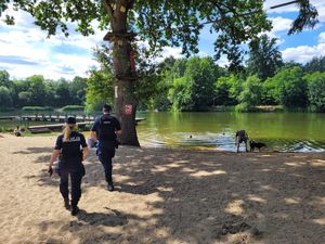 Policjant wraz z policjantką sprawdzają bezpieczeństwo osób korzystających z kąpieli w okolicznych jeziorach.