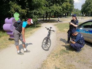 Policjant i policjantka w mundurach z napisem POLICJA sprawdzają rower mężczyzny stojącego nieopodal swojego jednośladu.