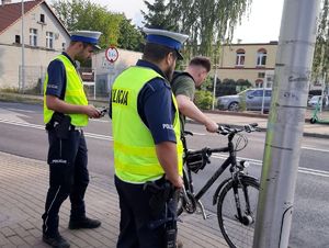 Dwóch policjantów w umundurowaniu z napisem POLICJA sprawdzają legalność jednośladów.