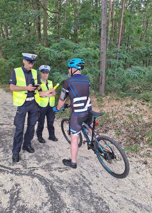 Policjant i policjantka w mundurach z napisem POLICJA rozmawiają z rowerzystą.