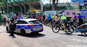 Policjantka w mundurze z napisem POLICJA stoi przy radiowozie policyjnym i pilnuje porządku przy rajdzie rowerowym.