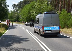 Kolizja drogowa na drodze krajowej. Na fotografii widoczny jest policyjny radiowóz, a w tle są strażacy.