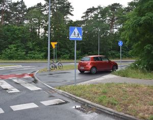 Czerwony samochód stoi na przejściu dla pieszych i rowerzystów.