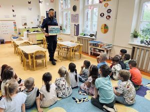 Policjant w mundurze z napisem POLICJA przedstawia grupie dzieci zasady bezpieczeństwa nad wodą.