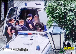 Trzech policjantów w mundurze z napisem POLICJA zatrzymali mężczyznę. Mężczyzna jest skuty kajdankami.