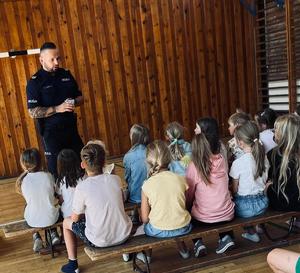 Policjant w mundurze z napisem POLICJA rozmawia z grupą dzieci.